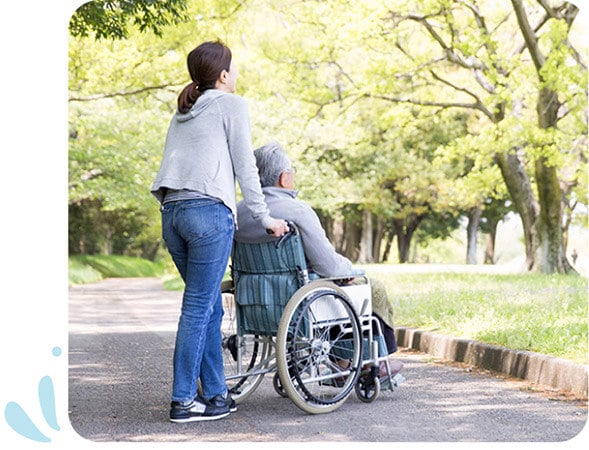 Care worker pushing wheelchair through park