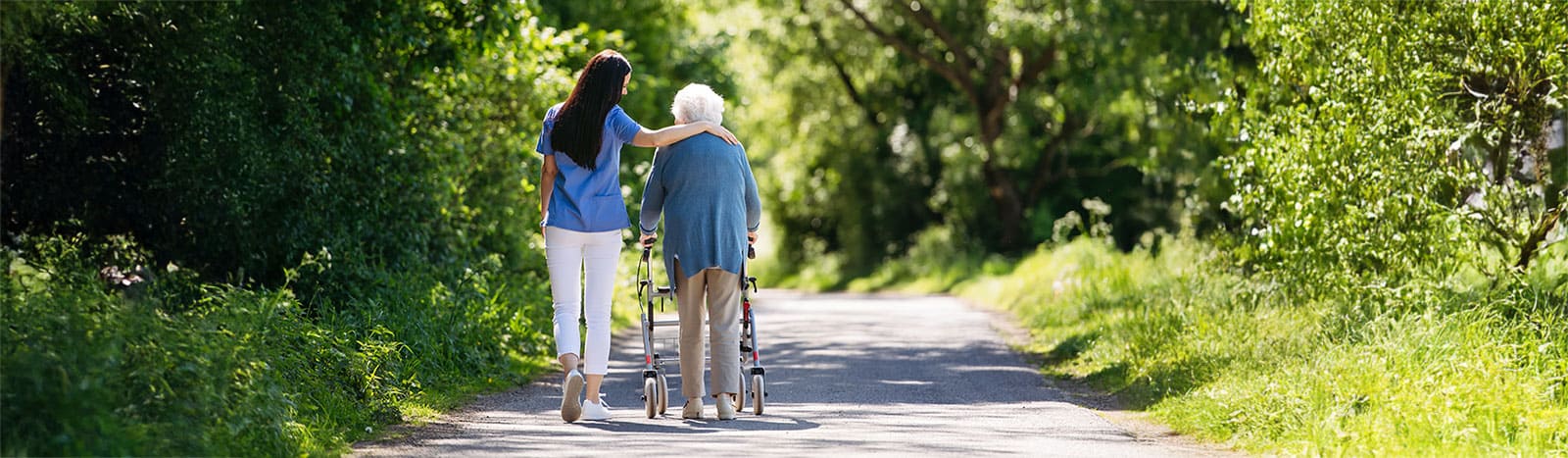 Care worker and elderly woman walking in the park on a sunny day